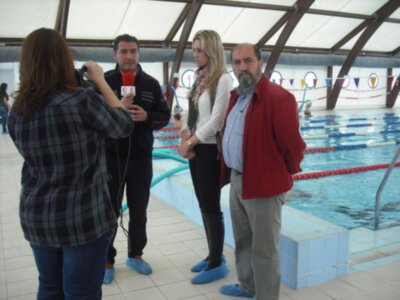 Entrevista en una piscina cubierta, con personas en trajes de baño y entrevistadora con micrófono.
