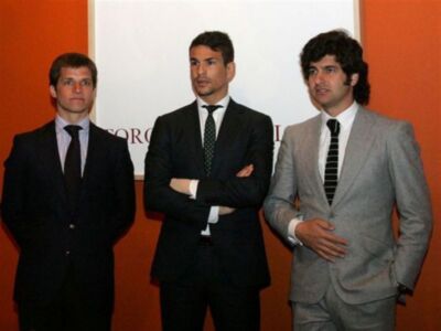 Tres hombres vestidos con trajes de negocios posan en una presentación formal.