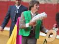 Un torero celebra con un ramo de flores y un sombrero en una plaza de toros.