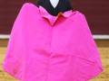Un torero en traje negro y camisa blanca sostiene un capote de color rosa brillante, preparándose para la corrida de toros en una plaza de toros.