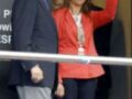 Dos personas, una con corbata y otra con chaqueta roja, saludando desde un balcón. Detalles de la imagen: corbata azul, chaqueta roja con cuello blanco y flecos, flores en el fondo.