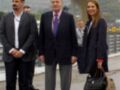 En una imagen, tres personas posan en un área de aterrizaje. La persona central, vestida con un traje oscuro y corbata morada, parece ser de una posición de liderazgo. A su izquierda, un hombre con una camisa blanca y pantalones negros también posa junto a ella. A su derecha, una mujer con un abrigo negro y una chaqueta blanca sostiene una maleta. El fondo muestra un edificio de aterrizaje con una estructura curva y varios paneles de información.