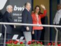 Una mujer con un vestido rojo y una corbata, junto a hombres en trajes, frente a un cartel de "BWT Gran Premio de España".
