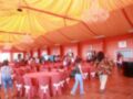 Una sala de fiestas con paredes rojas y techo amarillo, sillas rojas tapizadas, una mesa redonda, luces colgantes y una mujer caminando.