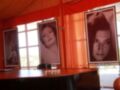 Una mesa con tres retratos de mujeres en marco, frente a una ventana con cortinas rojas.