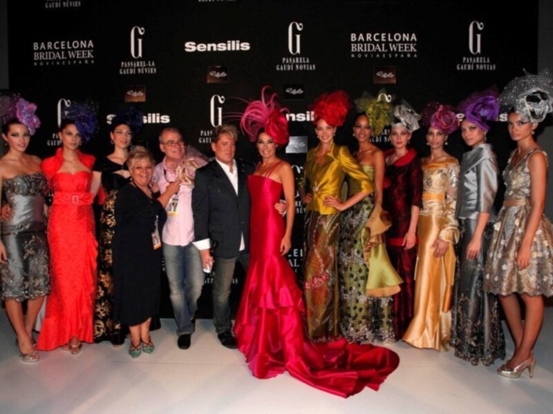 Una fila de modelos posando en la pasarela del Barcelona Bridal Week, con vestidos de colores vibrantes y accesorios elaborados.