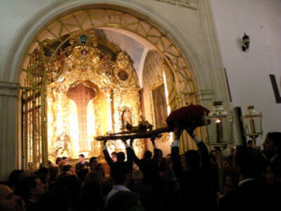 Una procesión religiosa en una iglesia con un altar dorado y una imagen central. La gente sostiene una estatua en el medio de la procesión.