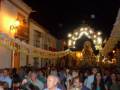 Festividad religiosa en un pueblo, con una procesión nocturna y una gran imagen de la Virgen iluminada por faroles.