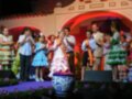Celebración cultural con niños en trajes tradicionales y adultos en un escenario festivo.