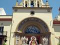 Imagen de una iglesia con una procesión religiosa, la Virgen del Carmen se encuentra en el altar. El cielo está nublado y hay gente participando en la celebración.