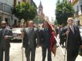 Una procesión religiosa en Sevilla, con hombres vestidos de gala y una cruz en mano.