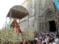 Procesión religiosa frente a la catedral, con una imagen venerada y flores en el centro.