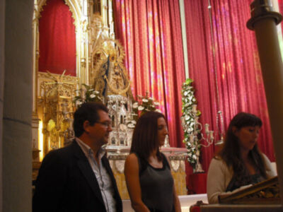 Una imagen de una iglesia con un altar dorado y una Virgen en el centro, rodeada por personas que parecen estar en un evento religioso.