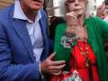 Un hombre y una mujer con vestimenta elegante y accesorios llamativos caminan juntos en una calle urbana.