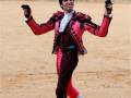 A matador in traditional pink and black attire, performing in a sandy arena with a crowd in the background.