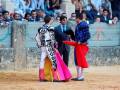 Toreros en una corrida de toros, con un toro en el fondo y espectadores detrás.