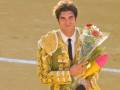 Un torero sonriente sostiene un ramo de flores, posiblemente en una plaza de toros.