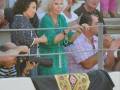 Una mujer con un vestido verde y una corona de flores, junto a otros espectadores en un evento deportivo.