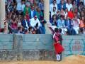 Un torero en traje tradicional se prepara para enfrentarse a un toro, mientras una multitud de espectadores observa desde la arena.