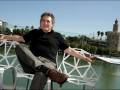 Hombre sentado en una silla moderna al aire libre, con el río Guadalquivir y la Torre del Oro de fondo.
