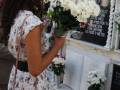 Una mujer deposita flores en un monumento funerario decorado con flores y un mensaje en un tablón de anuncios.