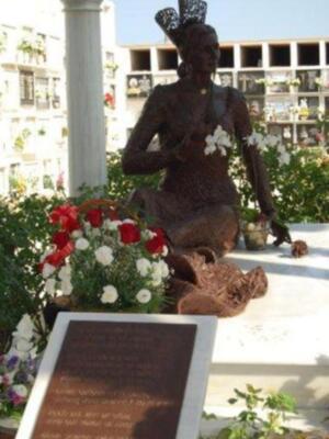 Estatua de bronce de una mujer sentada, adornada con flores blancas, en un entorno conmemorativo.