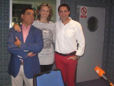 Tres personas posan en una sala con un microfono y un televisor.