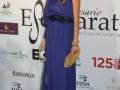 Elegant woman in a blue dress at a formal event with logos in the background.