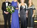 Una familia posa en una escalera, con un hombre en traje negro y corbata, junto a tres mujeres vestidas de noche. La escena parece ser formal o ceremonial.