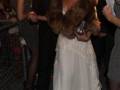 Una mujer vestida con un vestido blanco y una chaqueta de terciopelo marrón, posa para la cámara en un evento formal.