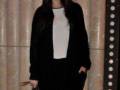 Elegante mujer con abrigo negro y falda blanca, sonriendo en un evento formal.