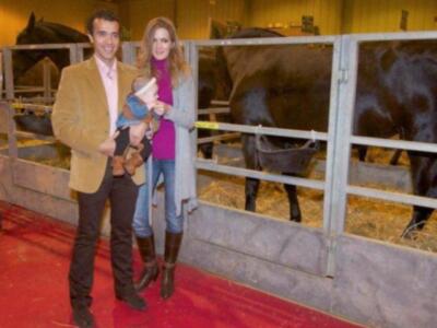 Un hombre y una mujer posan junto a un bebé en un corral de ganado, rodeados por vacas. La imagen muestra una escena familiar en un entorno rural con animales y personas.