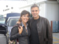 George Clooney y una mujer sonrientes, posando frente a un vehículo en un entorno urbano.
