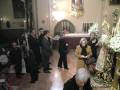 Celebración religiosa en una iglesia con personas en trajes formales y ofrendas florales.