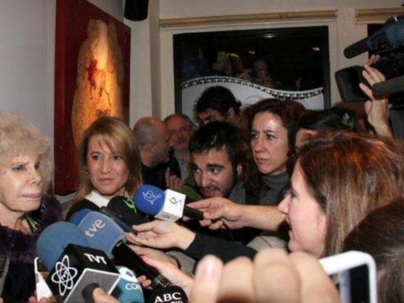 Una mujer hablando con una multitud de personas y microfonos en su frente.