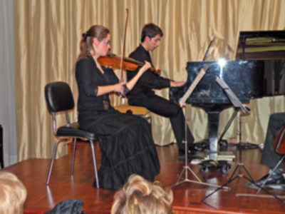 Dos músicos en un escenario, una mujer tocando violín y un hombre al piano.