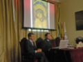Presentación en sala de conferencias con un hombre hablando frente a una pantalla que muestra un mosaico religioso.