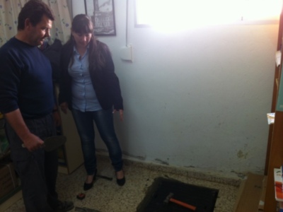 Un hombre y una mujer están en un cuarto con herramientas de construcción. La pared está despejada y hay una caja de herramientas en el suelo.