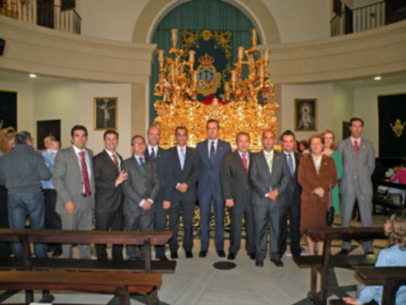 Grupo de personas posando en una sala con una gran imagen de un rey en el fondo.