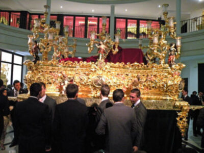 Una imagen de una iglesia con un altar dorado elaborado, rodeado por personas en trajes formales.
