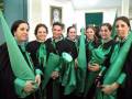 Una grupo de personas vestidas con trajes tradicionales verdes y negros, posando en un ambiente formal.