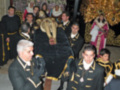Un grupo de personas vestidas con trajes ceremoniales, posiblemente de la orden de Malta, rodean una figura en trono. La escena está ambientada en un entorno decorado con luces y adornos navideños, sugiriendo una celebración o ceremonia religiosa.