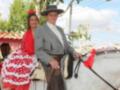 Fiesta tradicional con pareja vestida de traje de flamenca y traje típico andaluz, montando un caballo blanco.