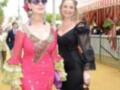 Dos mujeres posan en un ambiente festivo, una con vestido rosa y la otra con negro. Detalles como joyas y sombrillas sugieren un evento cultural o tradicional.