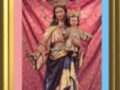 Imagen de la Virgen con el Niño Jesús, adornada con una corona y vestimentas doradas, enmarcada con colores rosado y azul.