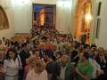 Una multitud de personas en una iglesia, algunos con vestimentas formales y otros más informales. La imagen muestra un ambiente de celebración o reunión religiosa, con gente de diferentes edades y estilos vestidos. La decoración interior sugiere un lugar histórico o de gran importancia religiosa.