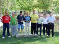 Ganadores del torneo de golf en un campo verde con árboles al fondo.