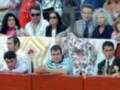 Spectators at a traditional bullfighting event, dressed in traditional attire, watching the event from behind a red barrier.