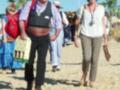 Una pareja caminando en una playa, con la mujer llevando un sombrero y el hombre un chaleco y un sombrero de vaquero.