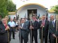 Un grupo de hombres en trajes y corbatas, algunos con insignias doradas, posan frente a una iglesia. La imagen muestra detalles de la celebración religiosa o festiva en curso, con un ambiente formal y ceremonial.